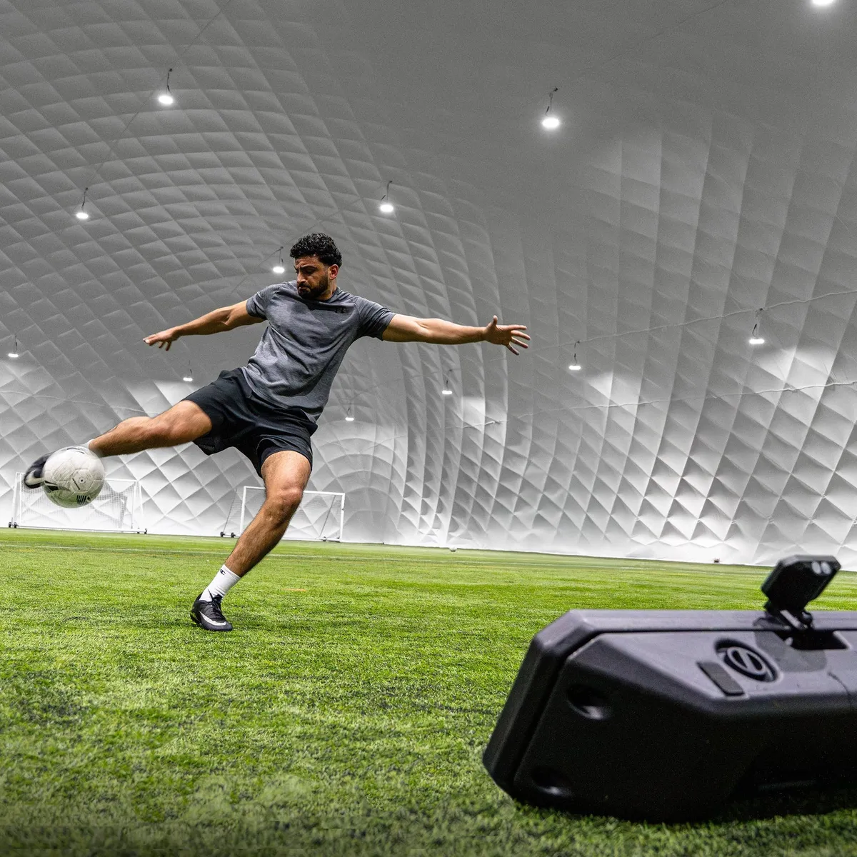 A player volleying a football towards a QUICKPLAY rebounder at an indoor pitch